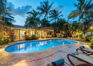 Backyard of rental with glowing pool after sunset, palm trees